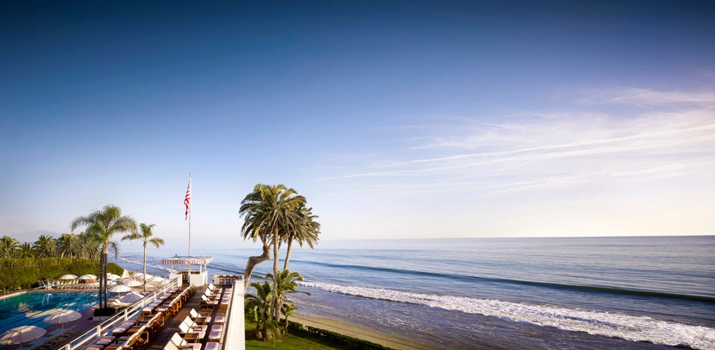 Spanish colonial-style luxury resort with white stucco walls and red tile roofs nestled among palm trees along Santa Barbara's coastline