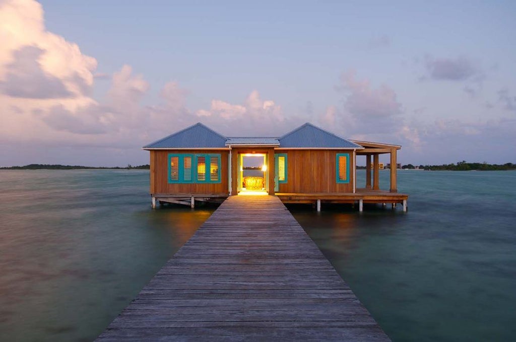 Secluded luxury villa with private dock extends over crystal-clear Caribbean waters, surrounded by lush palms at sunset in Belize