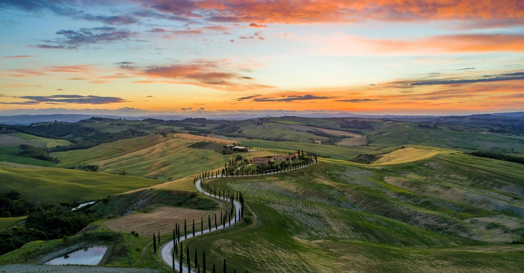 Luxurious historic Tuscan villa nestled among rolling green hills, stone facade glowing in warm golden sunlight with cypress trees surrounding the elegant property