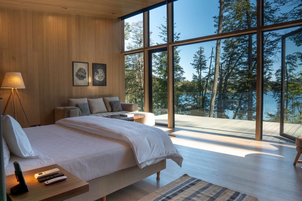 Luxurious lakeside villa with panoramic water views, elegant wood furnishings, and floor-to-ceiling windows overlooking Patagonian landscape at Las Balsas resort.