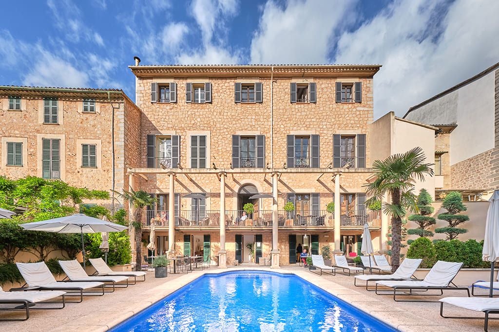 Luxurious Mediterranean-style hotel nestled in Sóller, Mallorca, with elegant stone facade, traditional shutters, and lush tropical garden terrace.