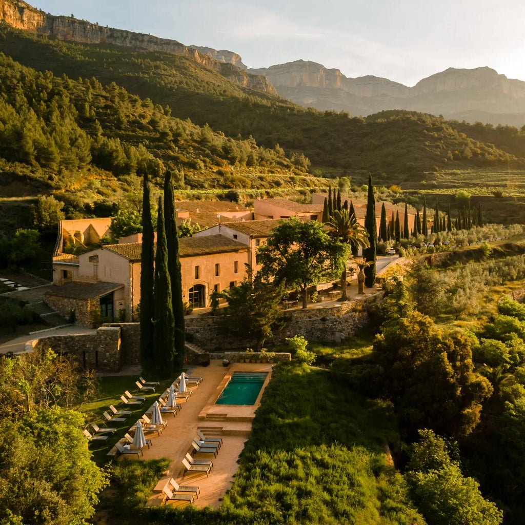 Luxurious stone winery hotel nestled in Spanish vineyard, with sun-drenched terracotta walls, elegant landscaping, and rolling hills in background