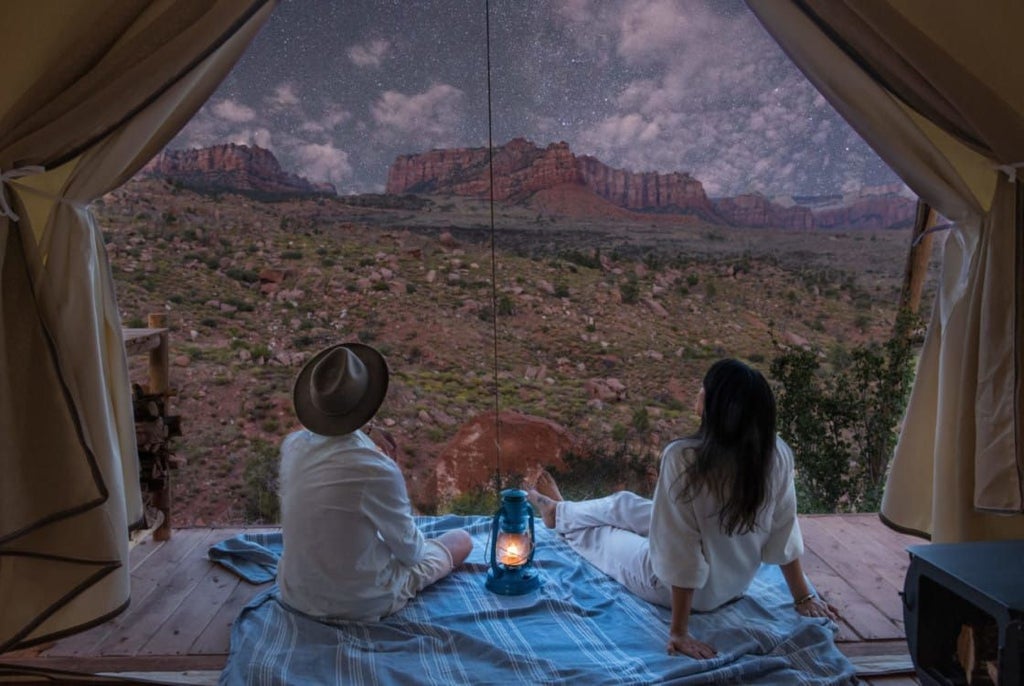 Luxury safari-style tent nestled against dramatic red rock cliffs of Zion National Park, with golden sunset light illuminating canvas and rugged landscape