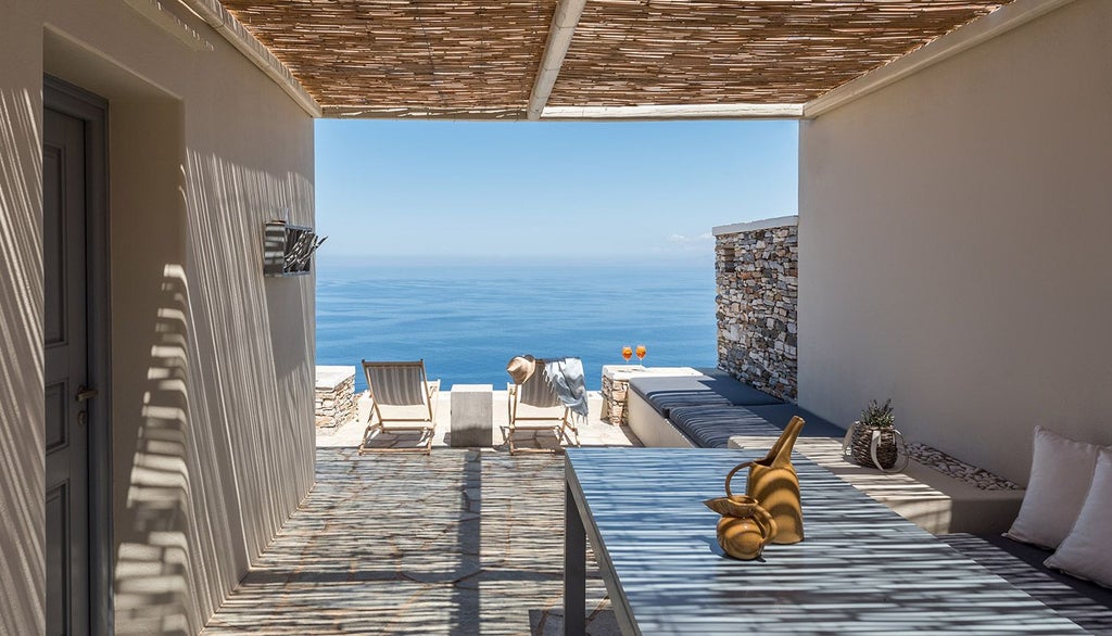 Elegant white-washed Cycladic hotel room with minimalist design, panoramic sea view, crisp linens, and soft natural light streaming across contemporary furnishings