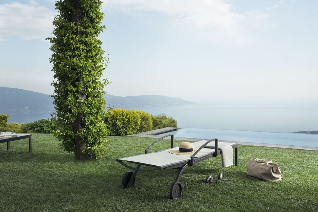 Modern infinity pool overlooking Lake Garda, with stone terrace and lounge chairs surrounded by mountains in misty golden light