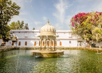 Opulent lakeside resort with grand white domed architecture, reflecting pools, and manicured gardens nestled amid Udaipur's mountains