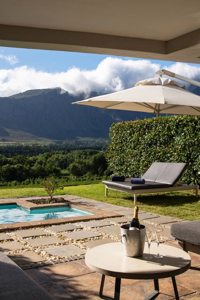 Luxurious CAP Classique Suite at Mont Rochelle hotel, featuring elegant decor, plush bedding, warm wood tones, and panoramic vineyard views in South African wine country