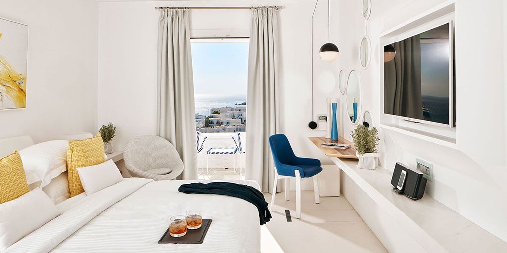 Luxurious white-washed hotel room with panoramic Aegean Sea view, minimalist design, private balcony, and elegant blue and white color palette reflecting Cycladic style