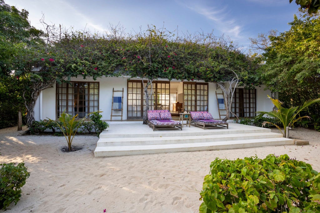 Luxurious beachfront bedroom at Kinondo Kwetu, Kenya, with wooden floors, white linens, and panoramic ocean view through large windows.