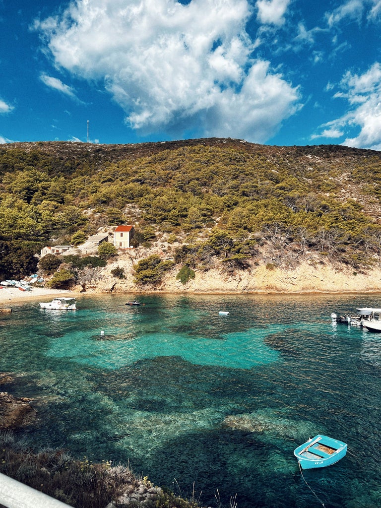 Traditional wooden boat with polished deck cruising crystal-clear turquoise Adriatic waters along Croatia's stunning rocky coastline