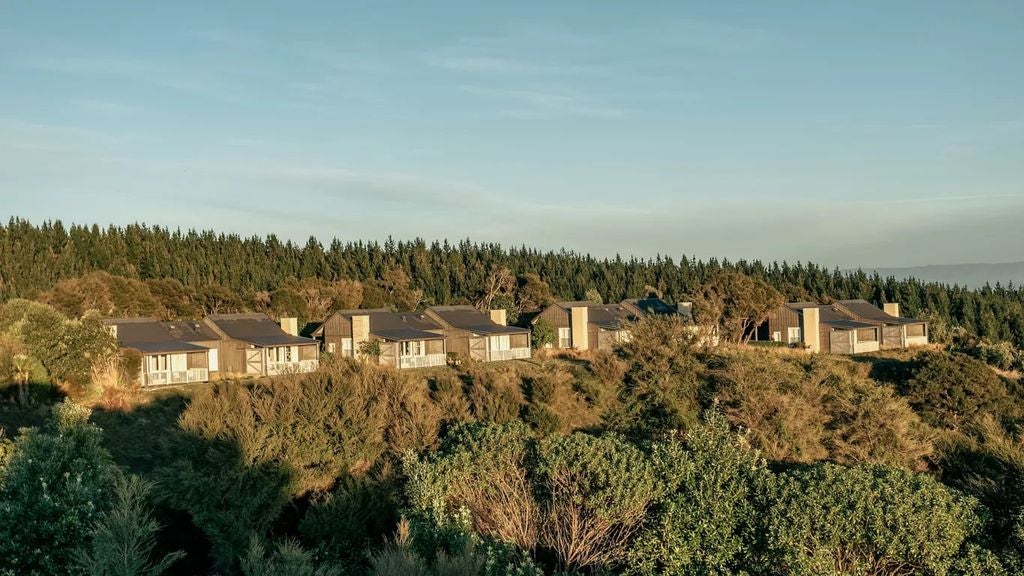 Spacious luxury suite with floor-to-ceiling windows overlooking rolling hills, featuring wood beam ceilings and rustic-elegant decor