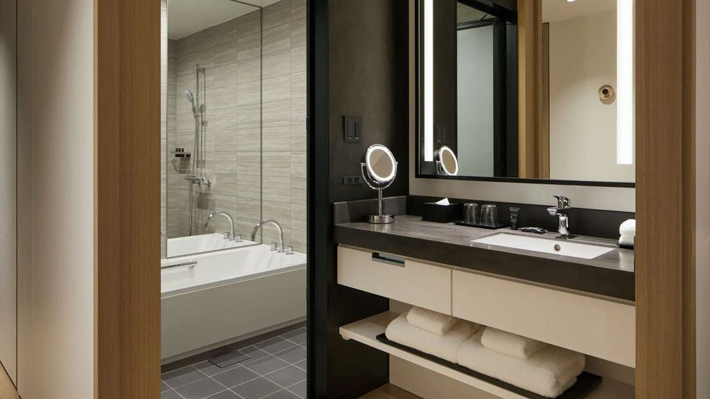 Modern hotel room with king bed, floor-to-ceiling windows overlooking Kanazawa city, minimalist decor, and warm wooden accents