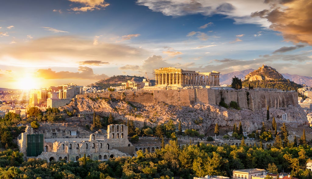 Ancient Parthenon temple illuminated at dusk on Acropolis hill, overlooking Athens cityscape with twinkling lights and Mediterranean sky