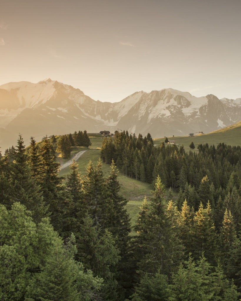 Luxurious alpine resort with snow-covered mountains, featuring stone and wood facade, private balconies and warm glowing windows at dusk