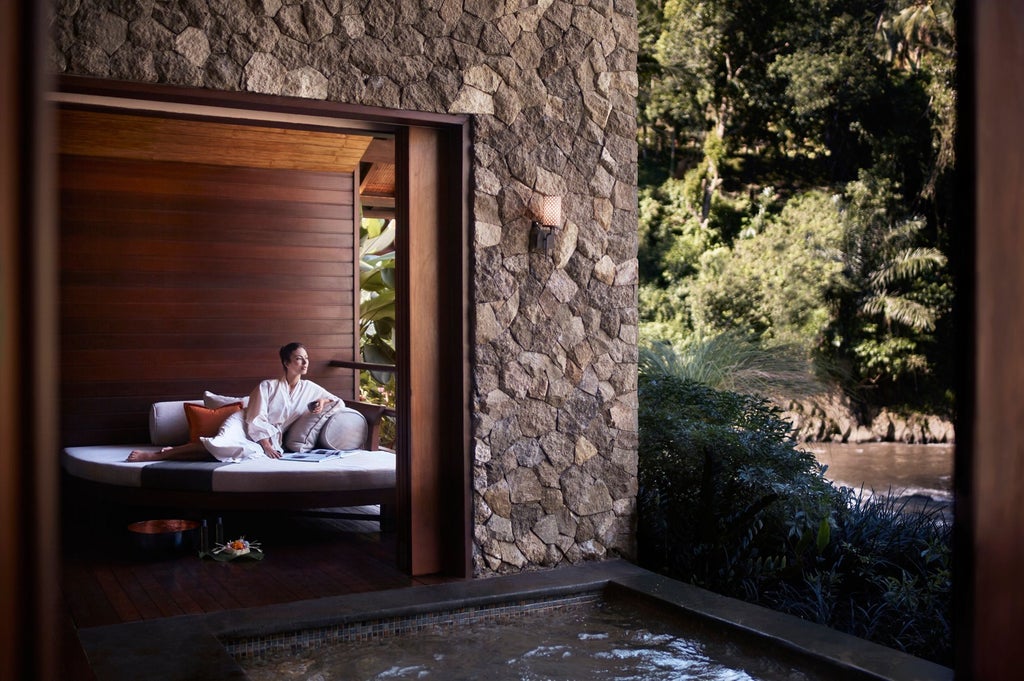 Luxurious infinity pool overlooking lush jungle valley at Ritz Carlton Mandapa Bali, with traditional Balinese architecture and palm trees