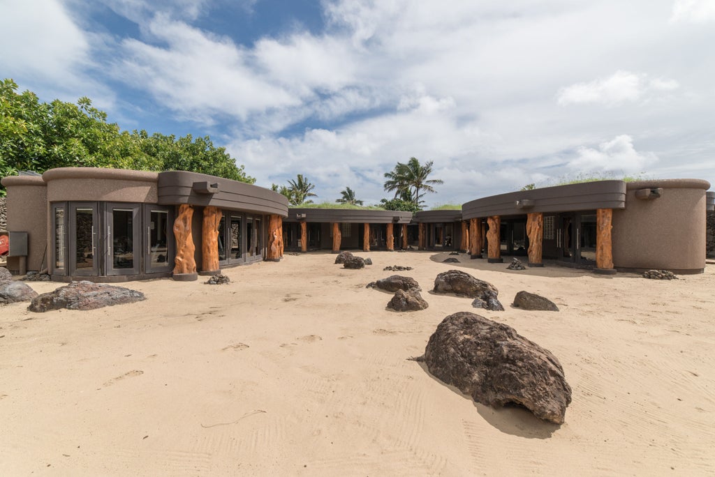 Luxury beachfront resort with curved stone architecture nestled into cliffside, overlooking Pacific Ocean at sunset on Easter Island