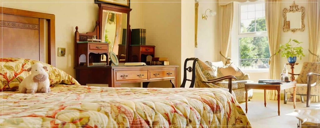 Elegant superior room in Park Hotel Kenmare, Ireland, featuring plush bedding, warm wood furnishings, and expansive windows overlooking lush landscape.