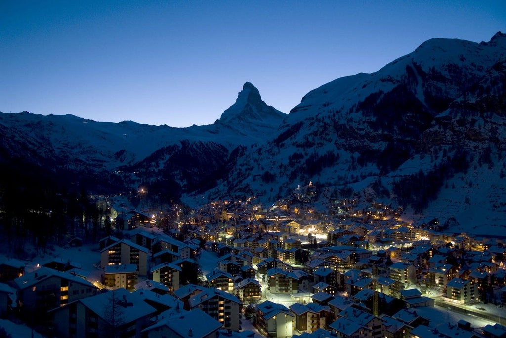 Modern luxury hotel exterior with angular glass architecture nestled in snowy Alps, Matterhorn peak visible in background