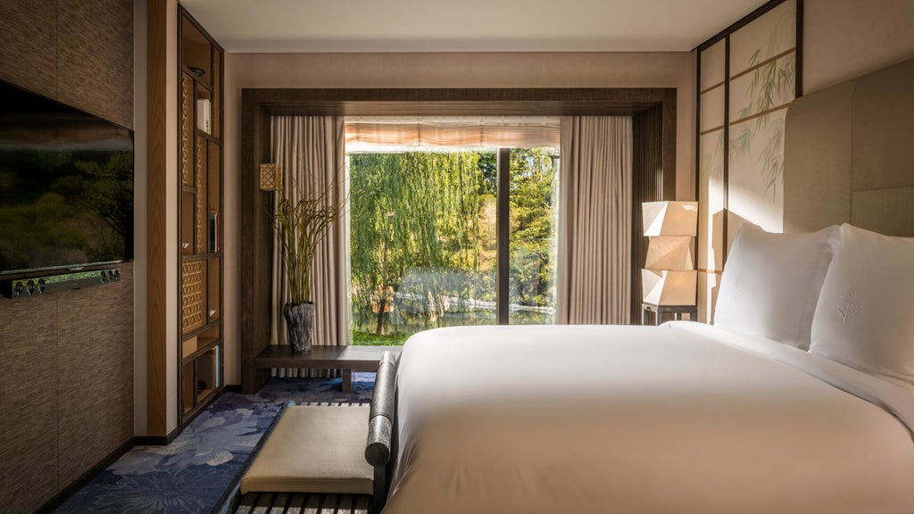 Elegant Japanese-style suite with wooden accents, tatami area, plush king bed, floor-to-ceiling windows overlooking garden pond