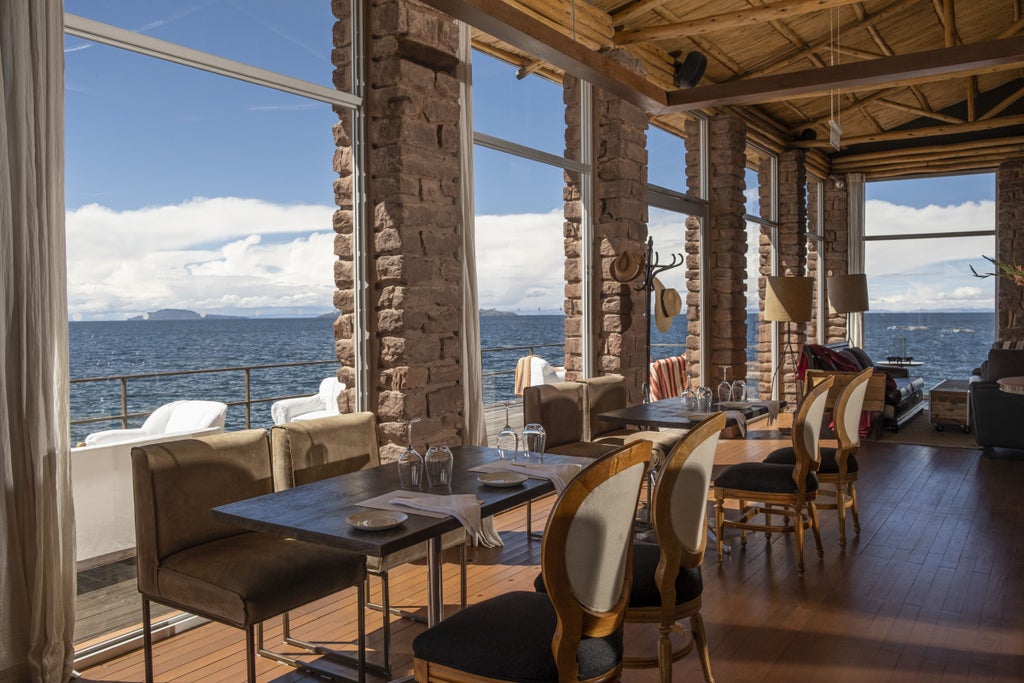 Stone luxury lodge with floor-to-ceiling windows overlooking Lake Titicaca, featuring modern architecture and waterfront terraces at sunset