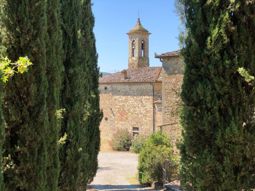 Historic Italian villa with stone facade, arched windows, and manicured garden courtyard nestled in rolling Tuscan countryside hills