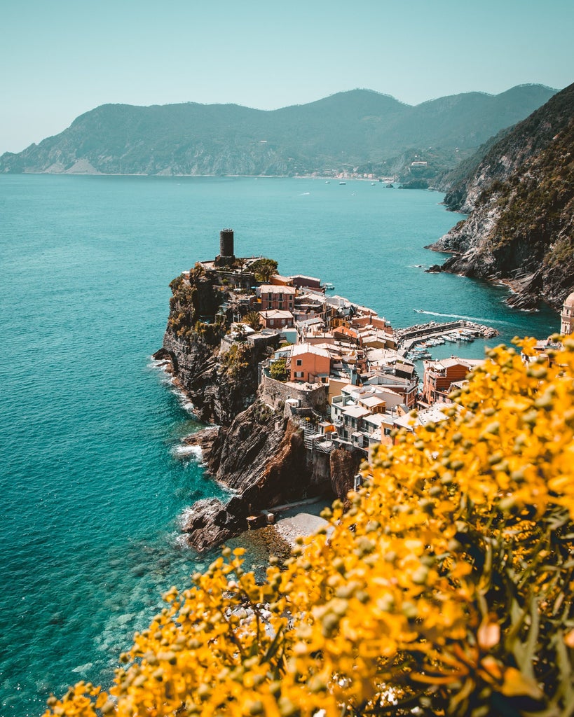 Colorful coastal houses perched on cliffs overlook turquoise Mediterranean waters in Cinque Terre's picturesque Manarola village