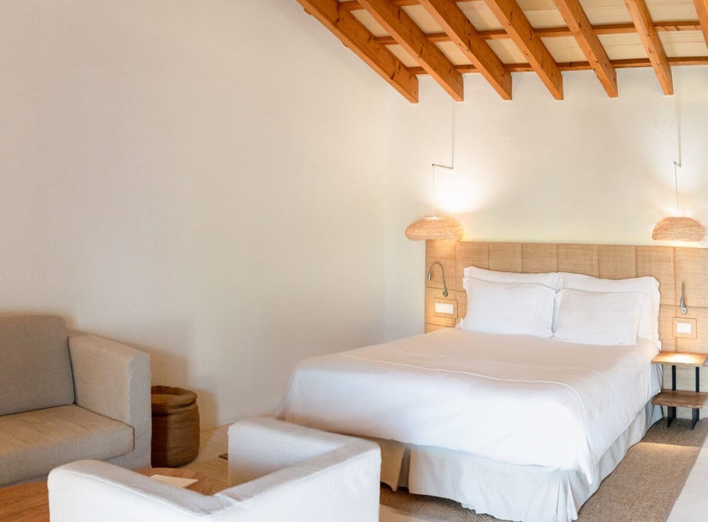 Minimalist luxury cottage interior with white walls, rustic wooden furniture, crisp linens, and panoramic view of Spanish countryside landscape