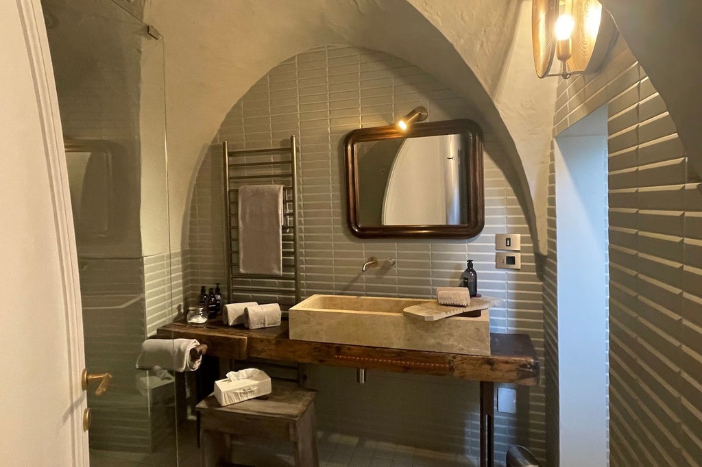 Elegant deluxe suite with ornate marble bathroom, plush white bedding, and panoramic windows overlooking historic Italian architecture in warm sunset tones