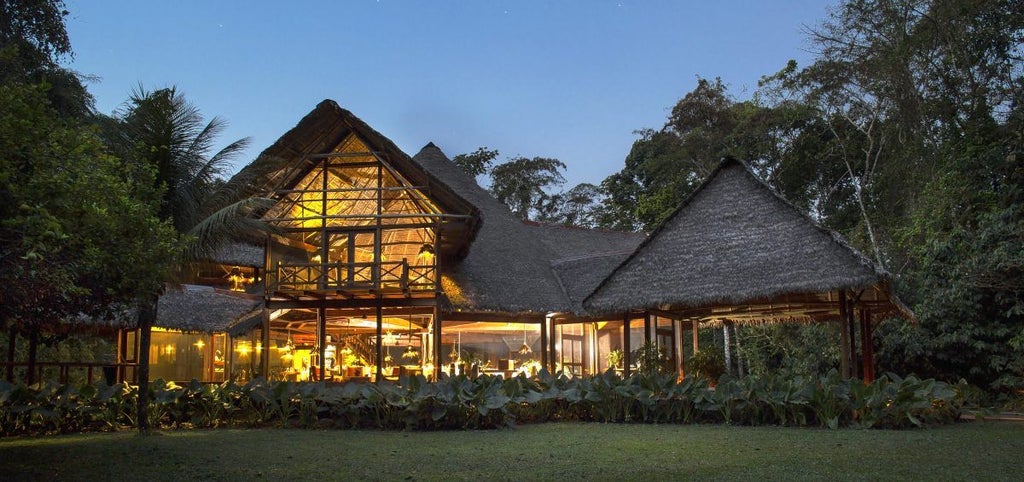 Elevated wooden walkways connect luxurious thatched-roof bungalows nestled in lush Peruvian rainforest canopy at sunset