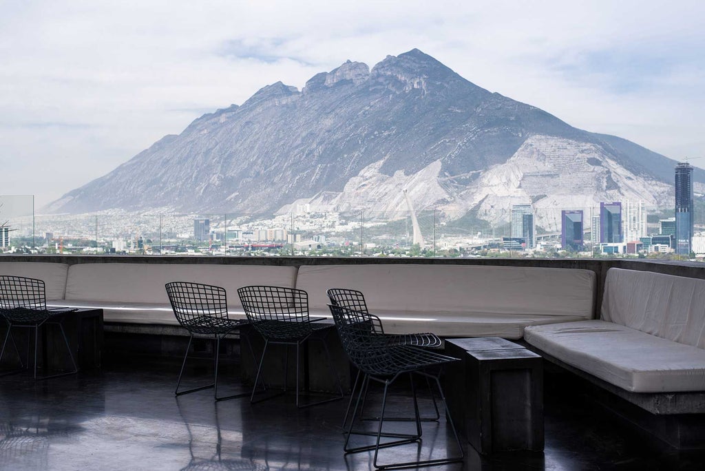 Modern glass-walled boutique hotel with sleek architectural design, minimalist white facade, situated in urban Monterrey skyline with mountain backdrop at dusk