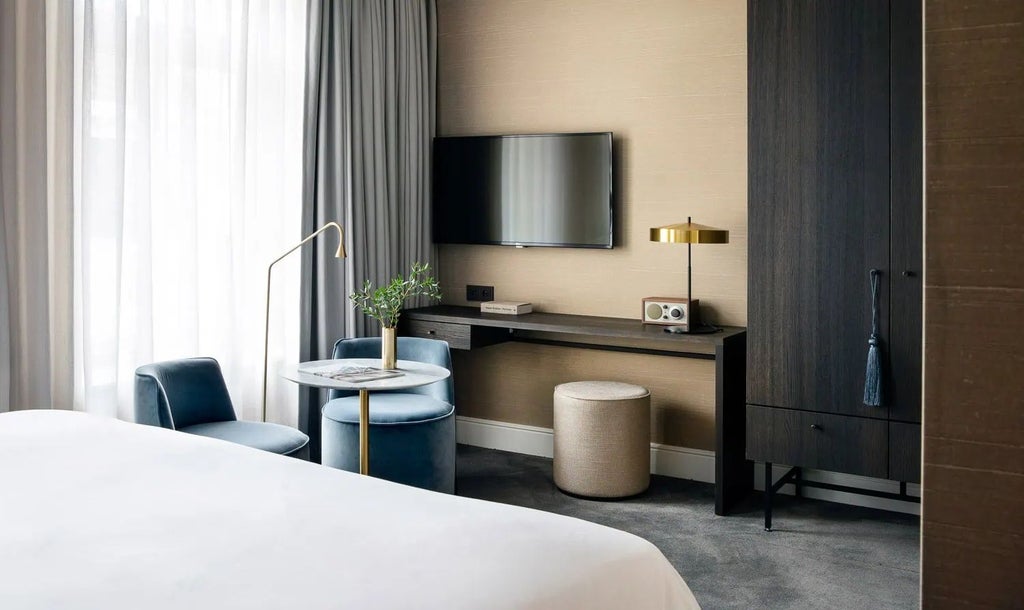 Elegant luxury hotel room with plush white bedding, refined furnishings, soft neutral tones, and sophisticated Belgian design aesthetics