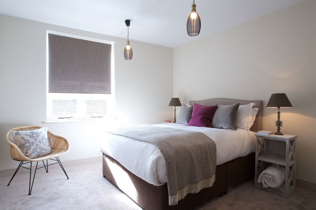 Spacious modern hotel suite with plush white bedding, elegant wooden furnishings, large window, and soft ambient lighting at Kings Head Hotel in the United Kingdom