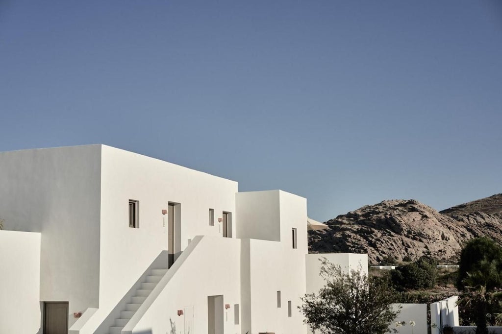 Minimalist luxury hotel with white stone archways, beige sun loungers, and crystal-clear pool surrounded by Grecian architecture