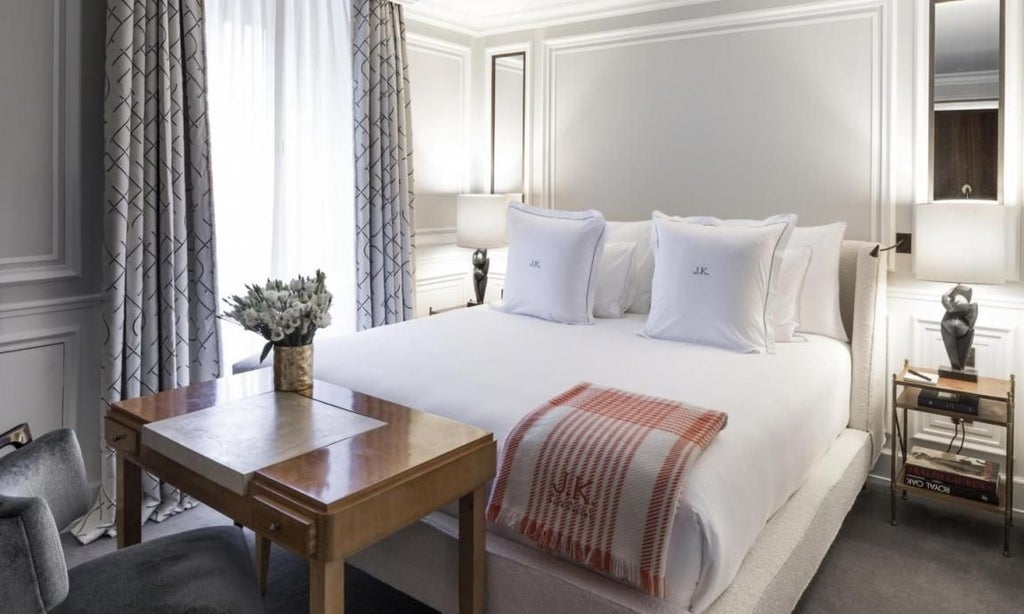 Elegant classic-style hotel room with soft neutral tones, plush white bedding, sophisticated artwork, and French-inspired refined interior design elements