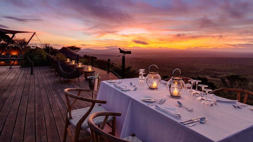 Luxury safari tents overlooking dramatic Kenyan landscape with rolling hills, wildlife-rich savanna, and distant mountain silhouettes at golden sunset.