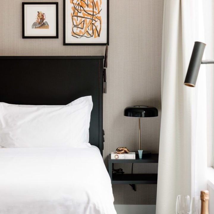 Elegant hotel room with plush white bedding, sleek modern furniture, soft lighting, and large windows overlooking urban scenset in Brussels centre.