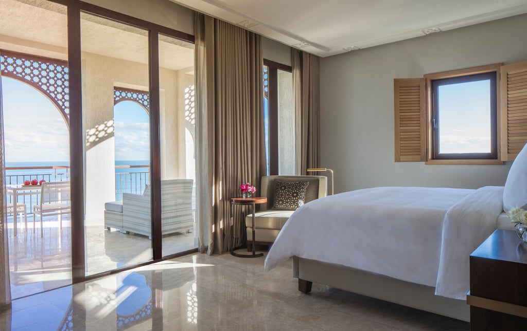 Elegant beachfront hotel with white Mediterranean architecture, palm-lined pools, and private balconies overlooking the Gulf of Tunis