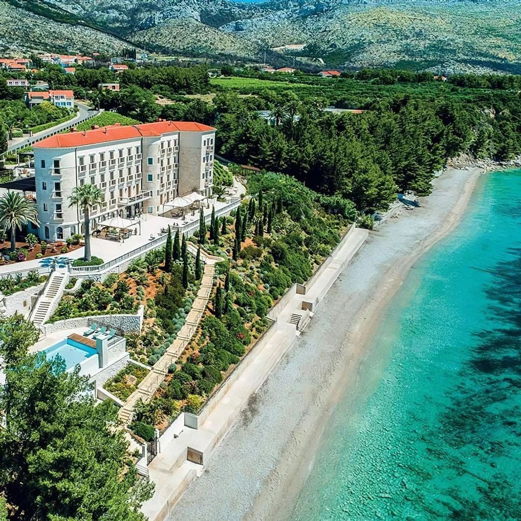 Elegant coastal villa with stone facade and red terrace, overlooking the Adriatic Sea, nestled among Mediterranean gardens in Croatia