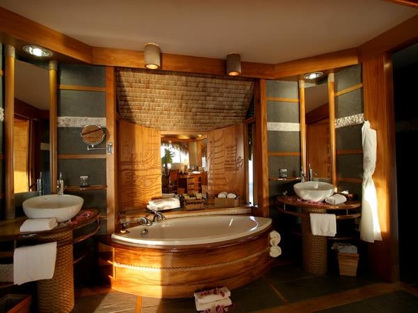 Luxurious overwater bungalow suite with private deck overlooking turquoise lagoon at sunset, featuring Polynesian-style thatched roof