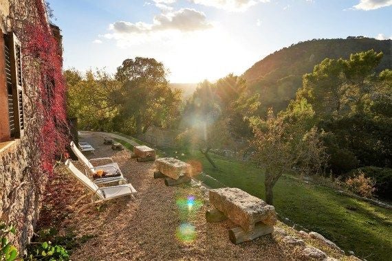 Luxurious stone facade of Hotel Mirabó nestled in Valldemossa, Mallorca, with sun-drenched terrace and historic Mediterranean architecture overlooking lush landscape