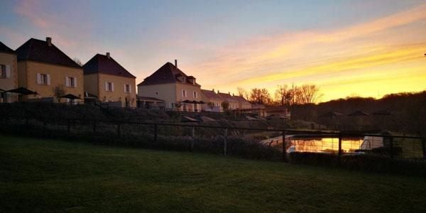 Elegant stone château with blue shutters nestled in lush French countryside, featuring manicured gardens and sun-drenched terrace under clear blue sky