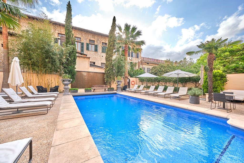 Elegant stone facade of luxurious boutique hotel in Sóller, Mallorca, with traditional Mediterranean architecture and lush green surroundings