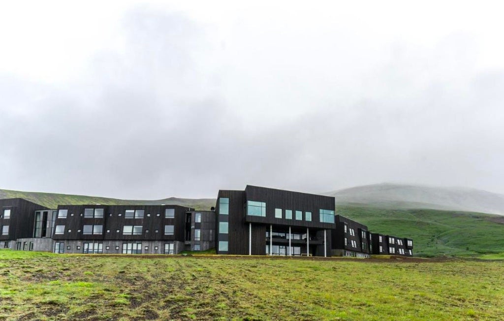 Modern minimalist hotel with glass facade nestled between mountains and ocean, reflecting Iceland's rugged landscape at sunset