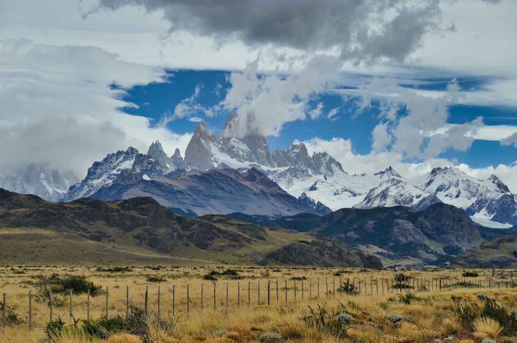 Snow-capped peak of Mount Fitz Roy rises above El Chalten village in Patagonia, with rustic wooden buildings nestled in autumn foliage