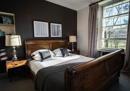 Elegant bedroom at Scenset House in Bainbridge, featuring plush white bedding, rustic wooden furnishings, and expansive countryside views through large windows.