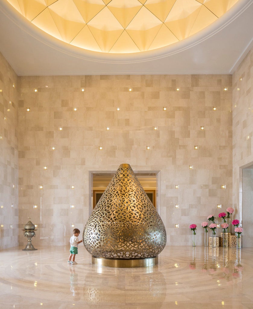 Elegant Mediterranean-style hotel with white arches and balconies overlooking a palm-lined beachfront pool and azure Tunisian coastline