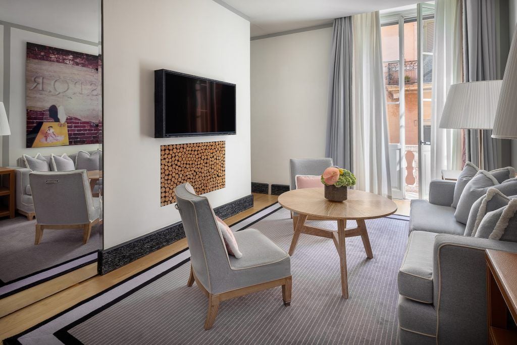 Elegant hotel room at Portrait Roma with plush cream-colored furnishings, soft lighting, and panoramic view of historic Italian architecture through large windows