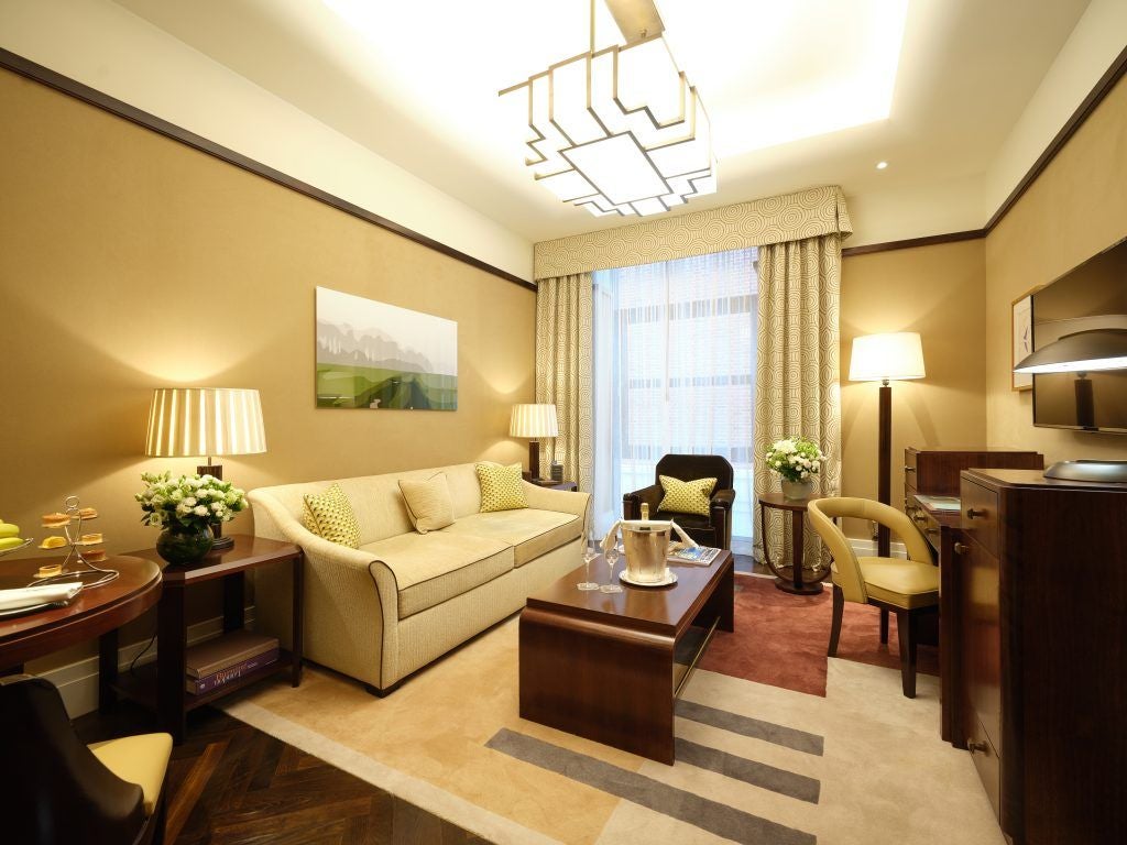 Elegant Mayfair Suite with plush king bed, contemporary art, soft neutral tones, and luxurious marble bathroom bathed in warm afternoon light