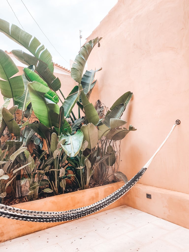 Minimalist stone archway frames sun-drenched Spanish courtyard with rustic wooden furniture and potted Mediterranean plants at Can Ferrereta