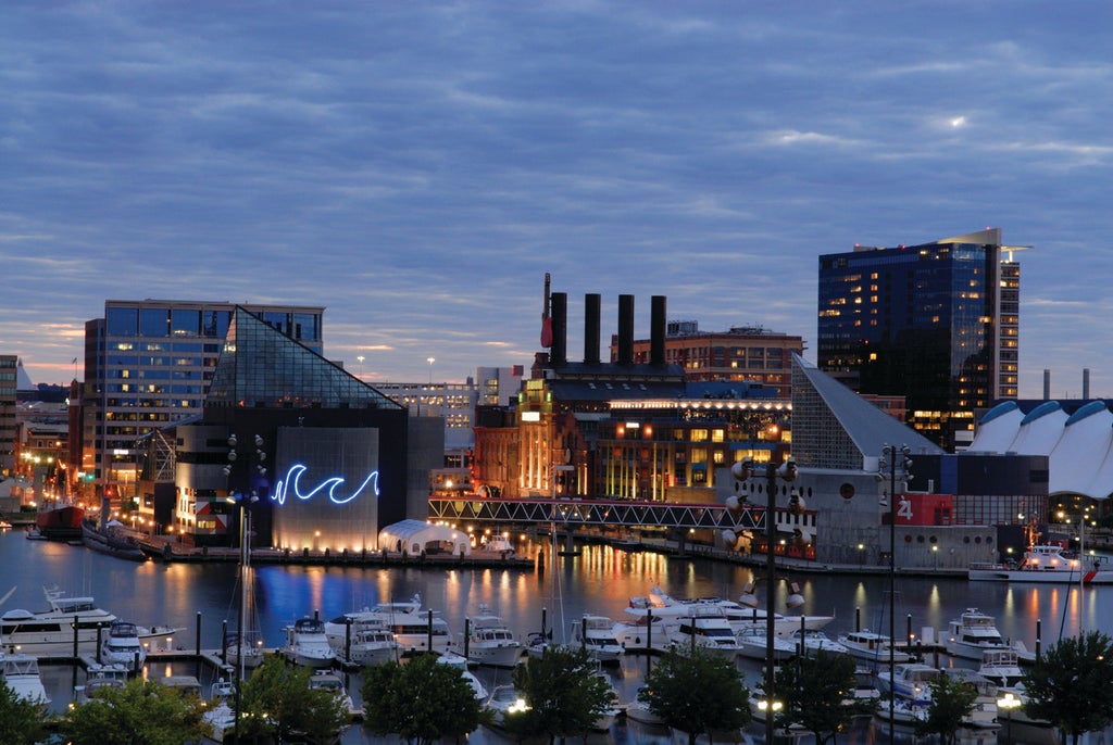 Waterfront luxury hotel tower in Baltimore with glass facade, reflecting sky and harbor, featuring elegant curved architecture.